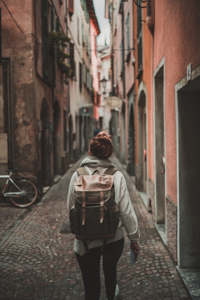 Woman, seen from the back, walking alone down a cobblestone street in Italy